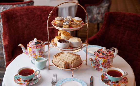 Afternoon tea at Thistle Marble Arch with a tiered stand of pastries, scones, and sandwiches, served with floral teapots and cups of tea
