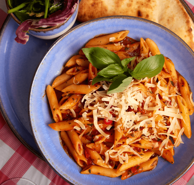 Top-down view of a plate of pasta with tomato sauce, grated cheese and basil