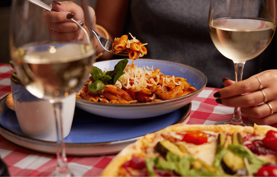 Pizza and pasta on a table with glasses of wine