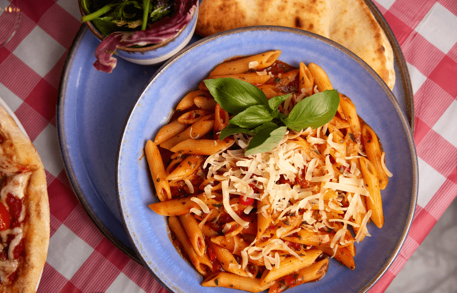 Top-down view of a plate of pasta with tomato sauce, grated cheese and basil