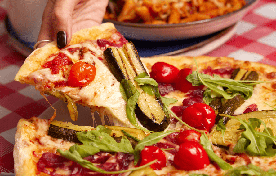 Hand pulling a pizza slice with cheese, tomatoes and courgettes as toppings