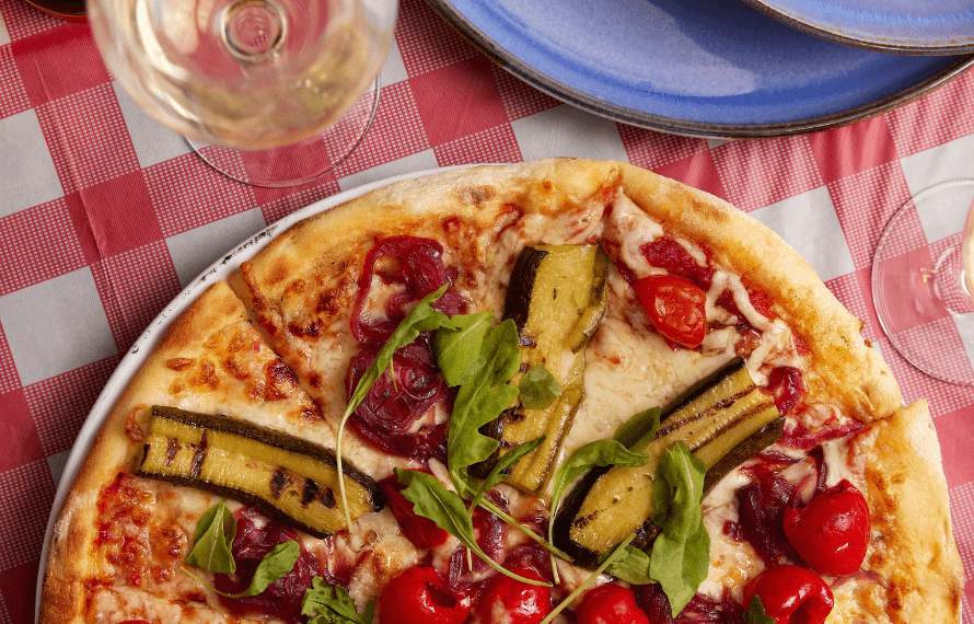Top-down view of a pizza with courgettes, cheese, tomatoes and rocket with glasses of wine