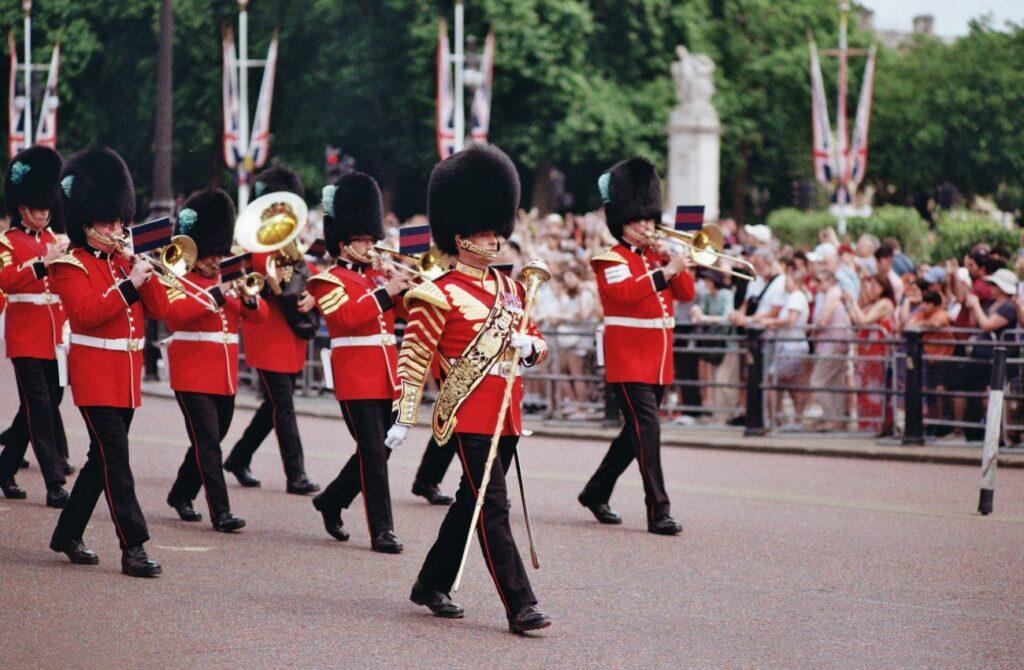 British guards in red uniforms march through London playing brass instruments during a ceremonial parade.