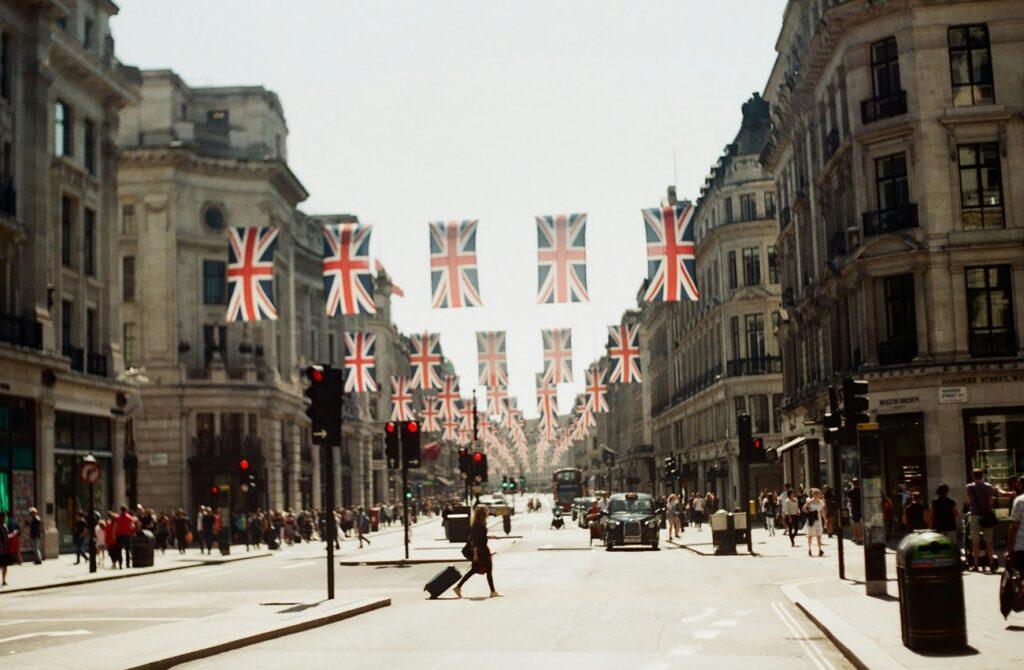London street lined with historic buildings and rows of Union Jack flags hanging overhead.