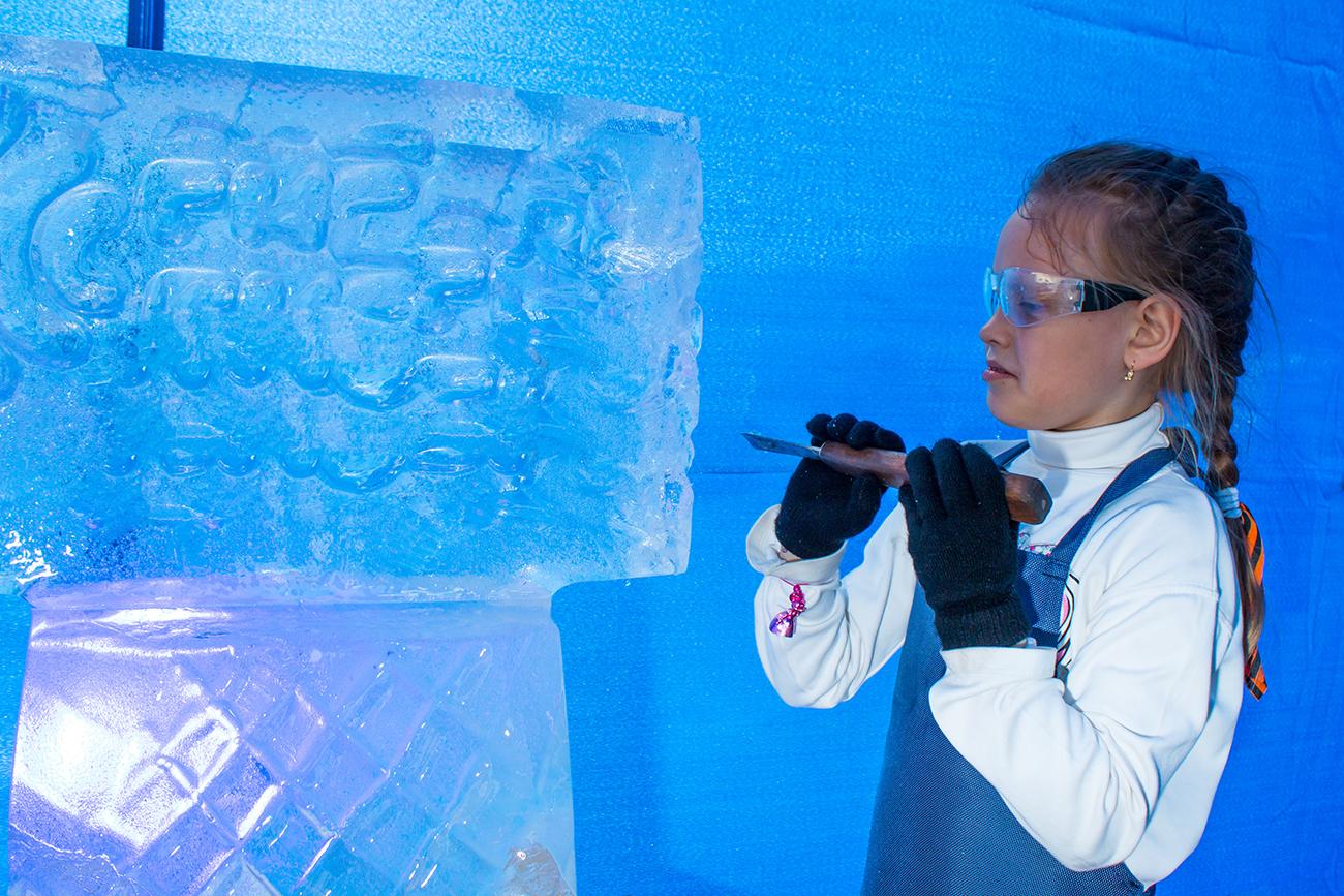 Girl of seven years in a master class on ice sculpture on a blue background